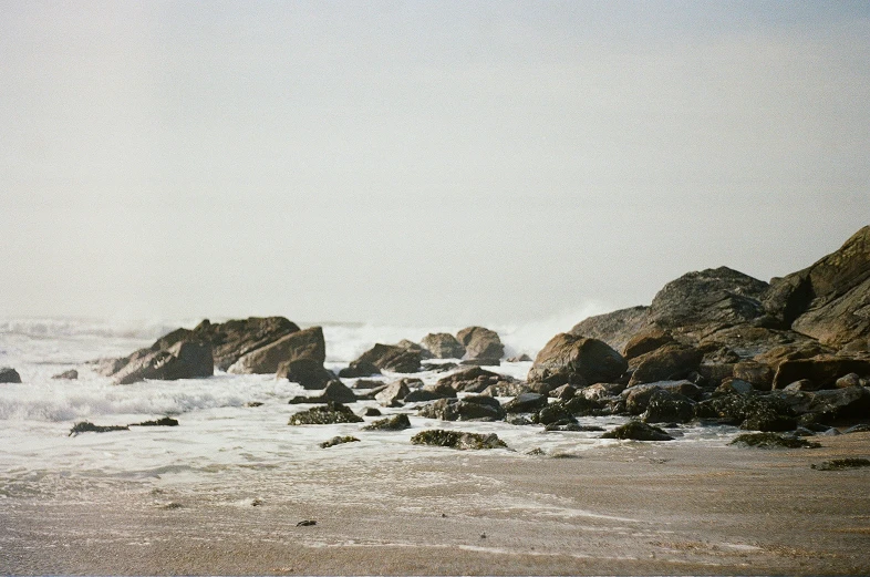 two people walking on beach next to some rocks