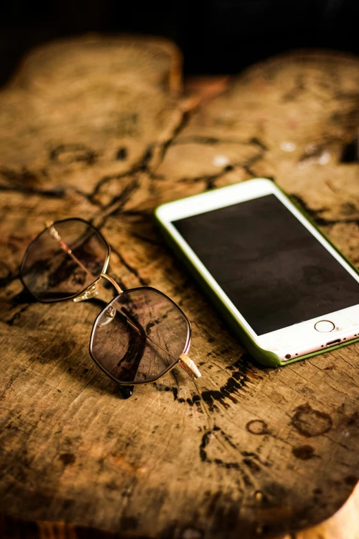 a wooden table with a cell phone and a pair of glasses