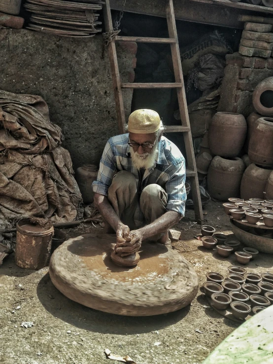 an old man sits making clay pots in his home