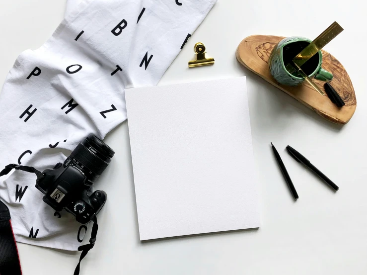 a notebook, camera, sunglasses, shoe and paper on a white surface