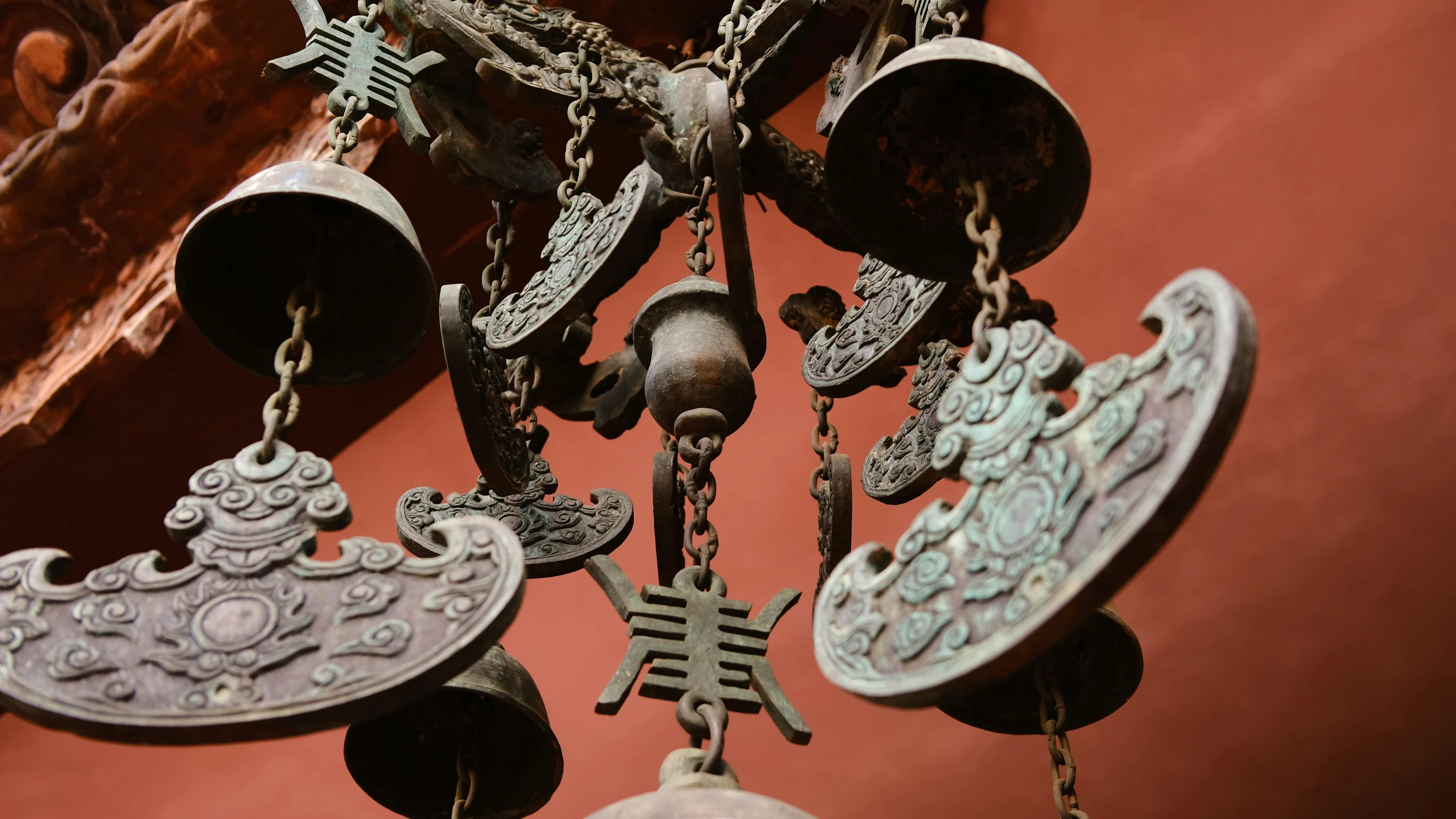 bells hang from chains near a red wall