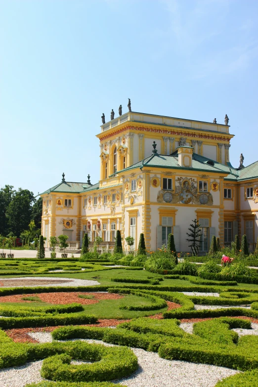 an elaborate orange and yellow building with hedges in front