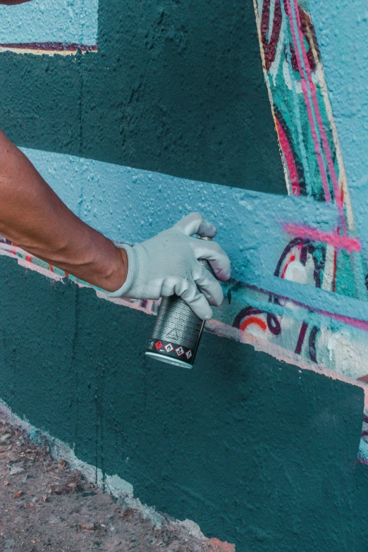 a man wearing white gloves spray painting on a blue wall