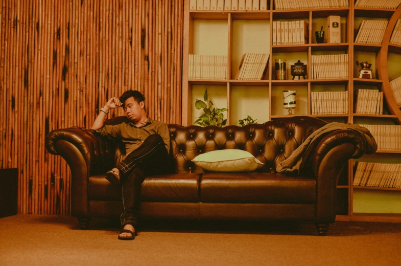 a young man sits in a brown leather couch