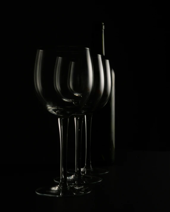 three wine glasses and a bottle sitting side by side on a table