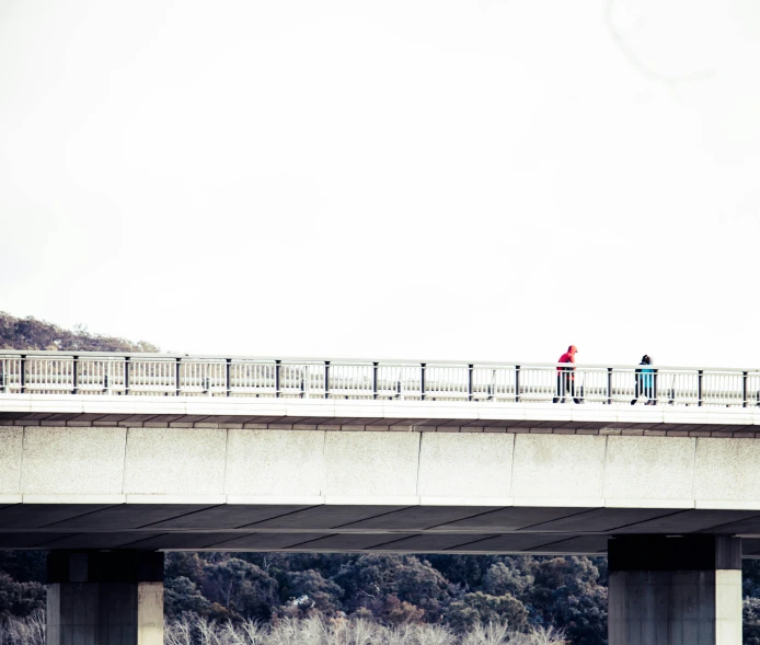 two people standing on a bridge, one with an umbrella