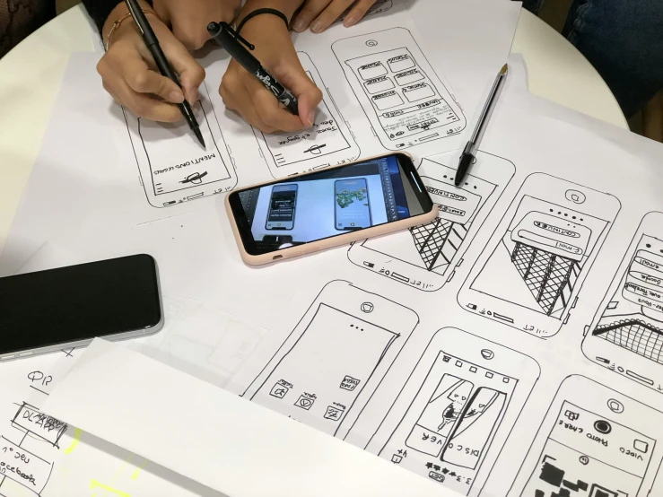 two people sitting around a table using pens to sketch an electronic device