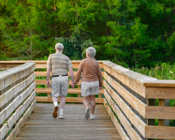 two elderly men walking on a wooden bridge