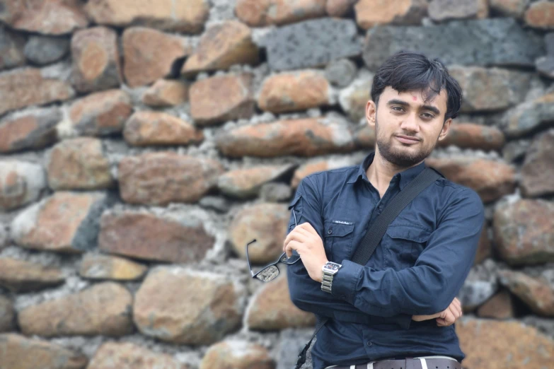 a man wearing a watch poses by a rock wall