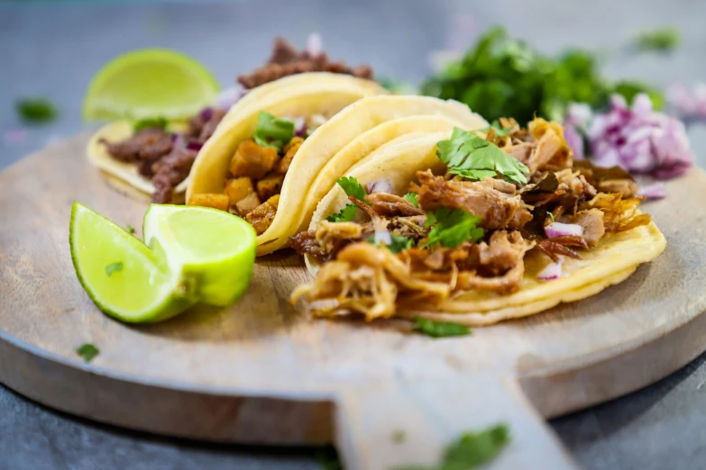 three tacos sit on a wooden board with green garnish