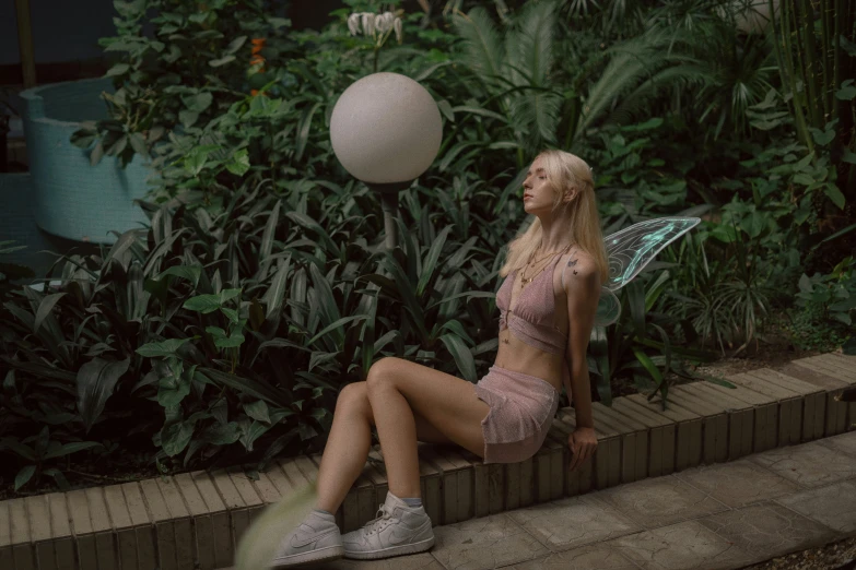 a young lady in pink swimwear sits on brick near a plant