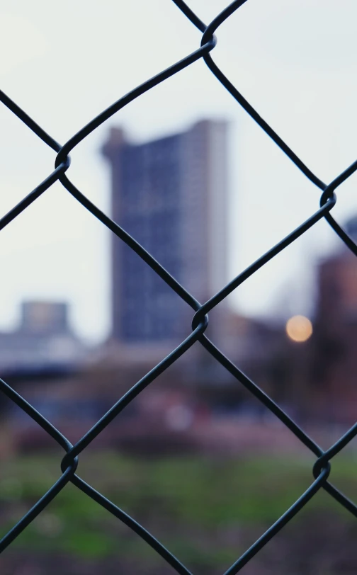 a fenced in area with a grassy area and tall buildings behind it