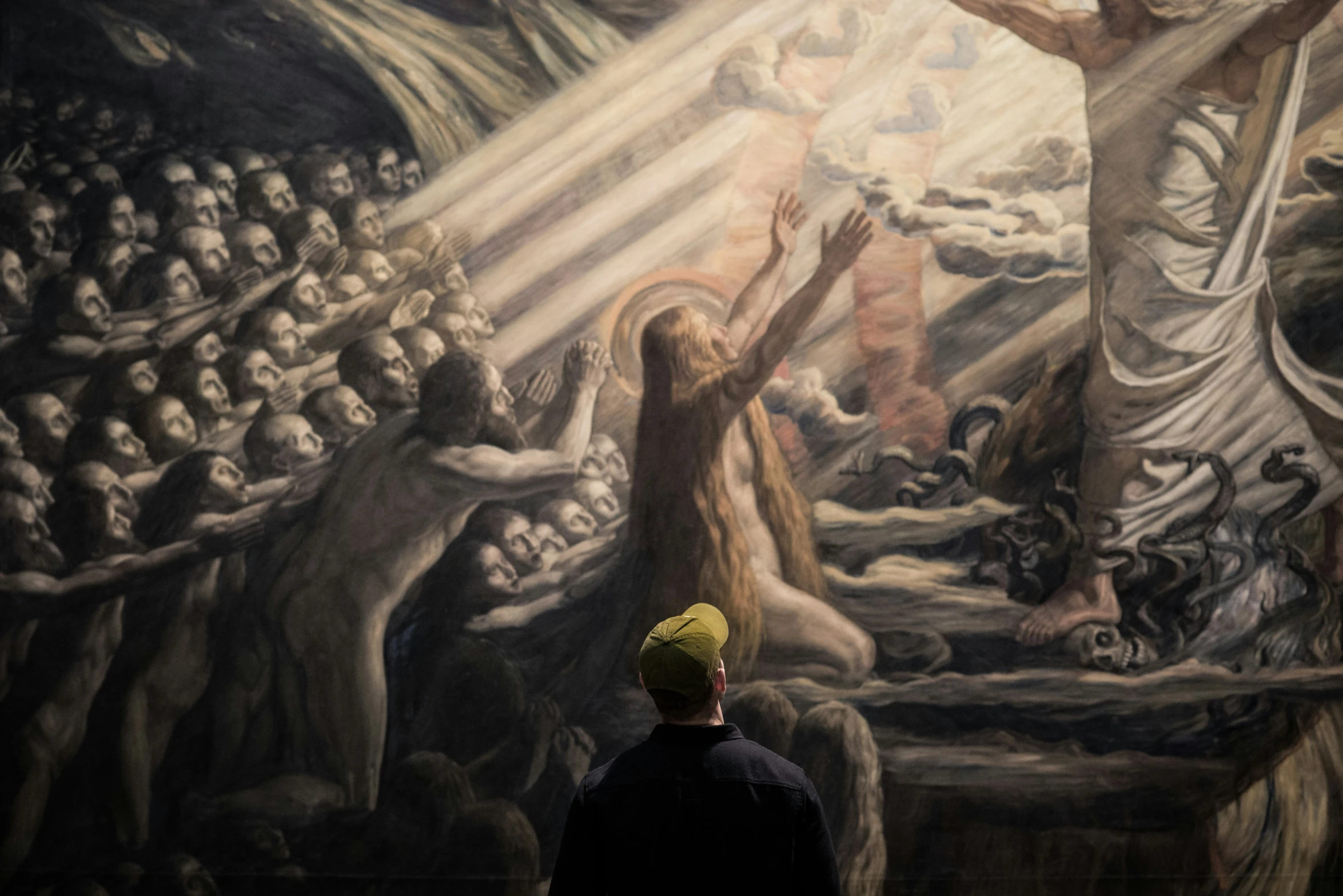 a person stands in front of a painting depicting angels and demons