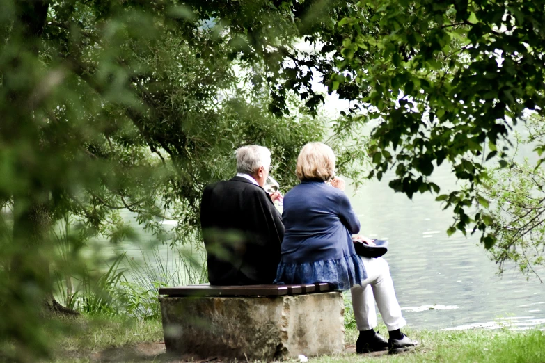two older people are sitting on a bench by the water