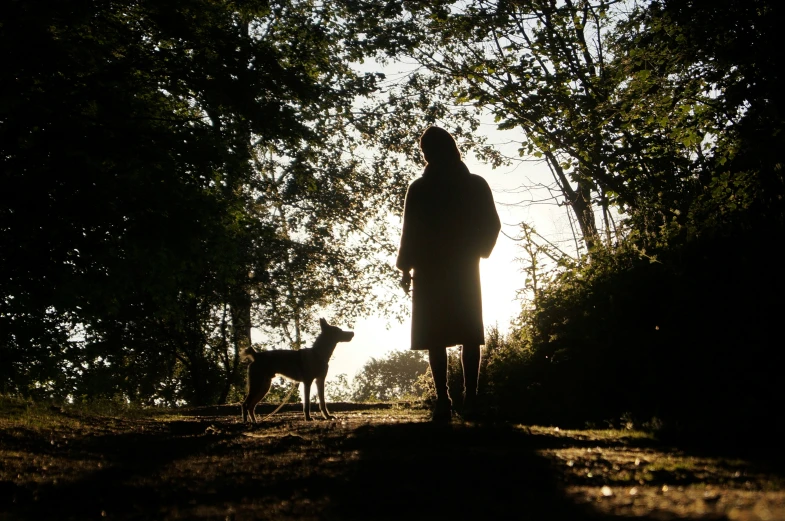 woman and dog standing outside in a forest at sunset