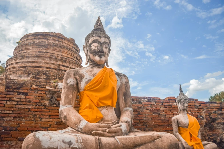 two statues of buddhas near brick wall with sky in background