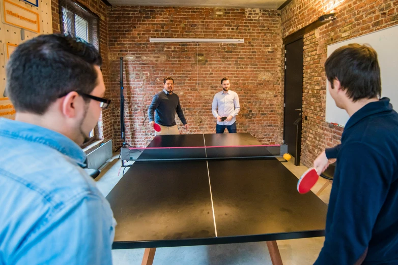 three young men playing table tennis together in a brick walled room