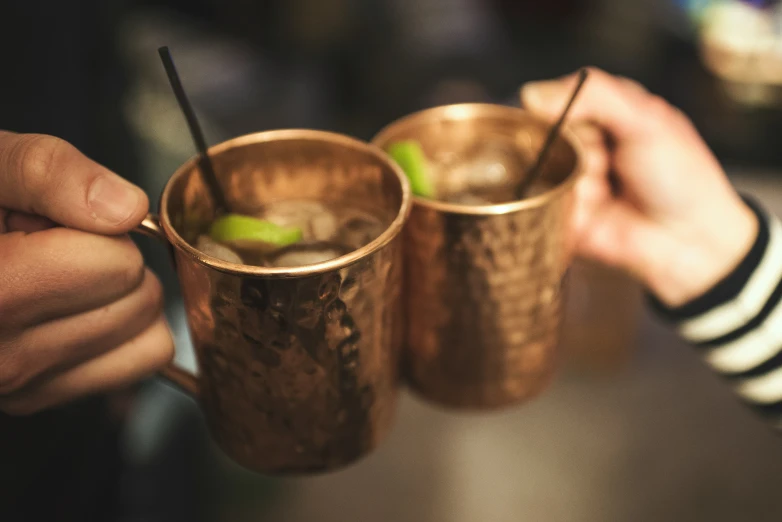 two cups with lids holding cocktails in their hands