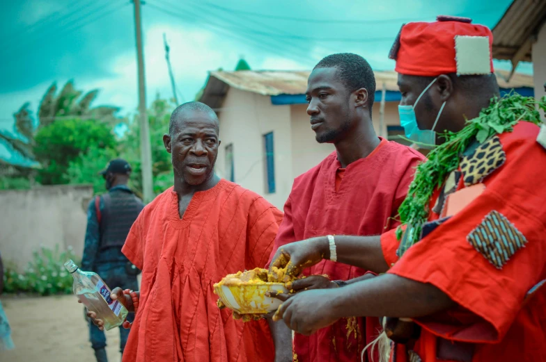 three men in red outfits standing and holding plates of food