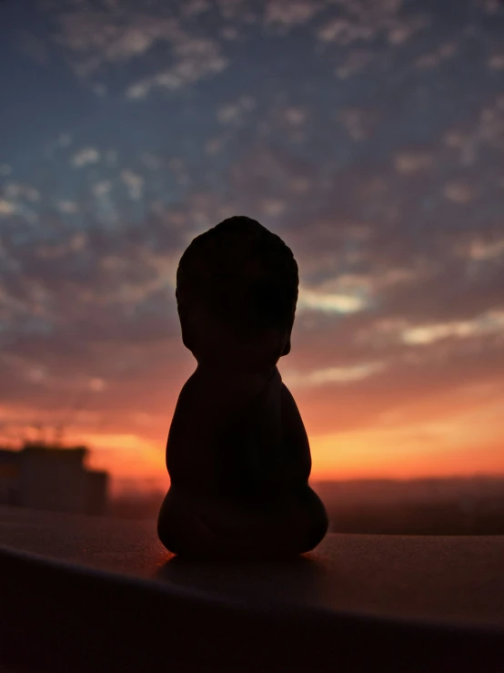 the sun is setting in a cloudy sky behind a small teddy bear