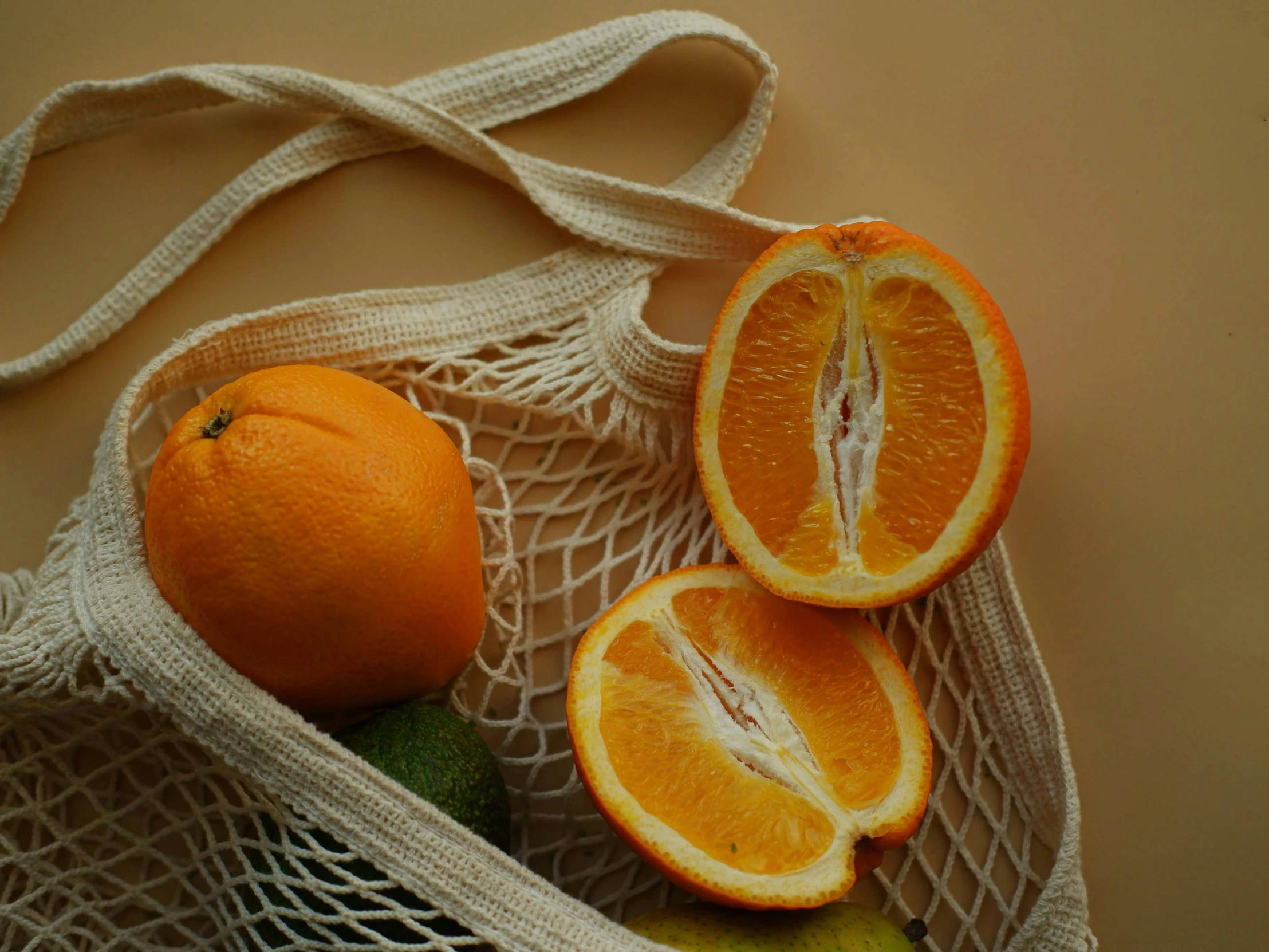 three oranges in a net bag with one sliced off