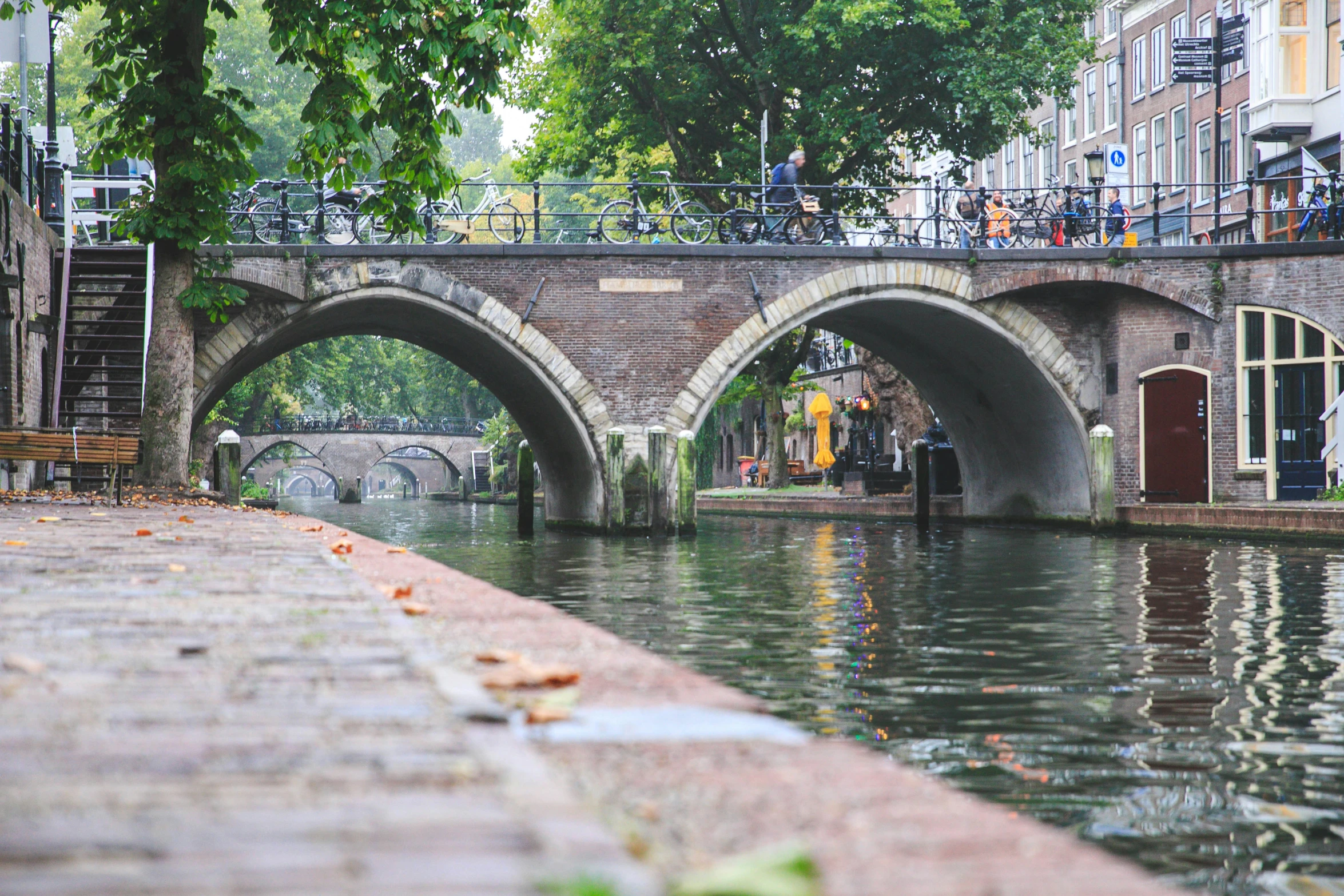 a river flowing under a brick bridge next to tall buildings