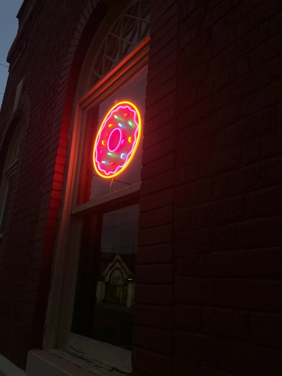 an illuminated neon doughnut on a red brick wall