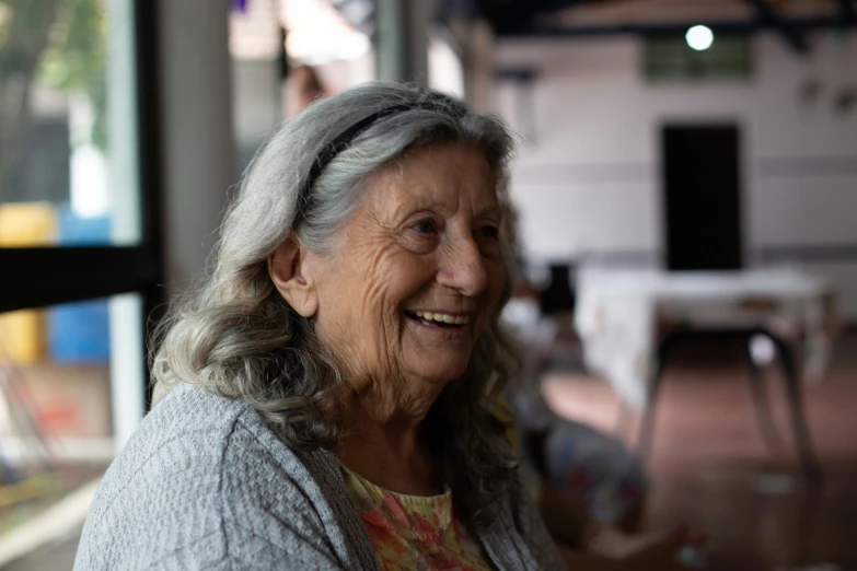 an old lady smiling at the camera while she sits at a table