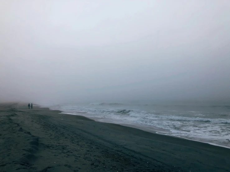 foggy beach with people walking along the shoreline