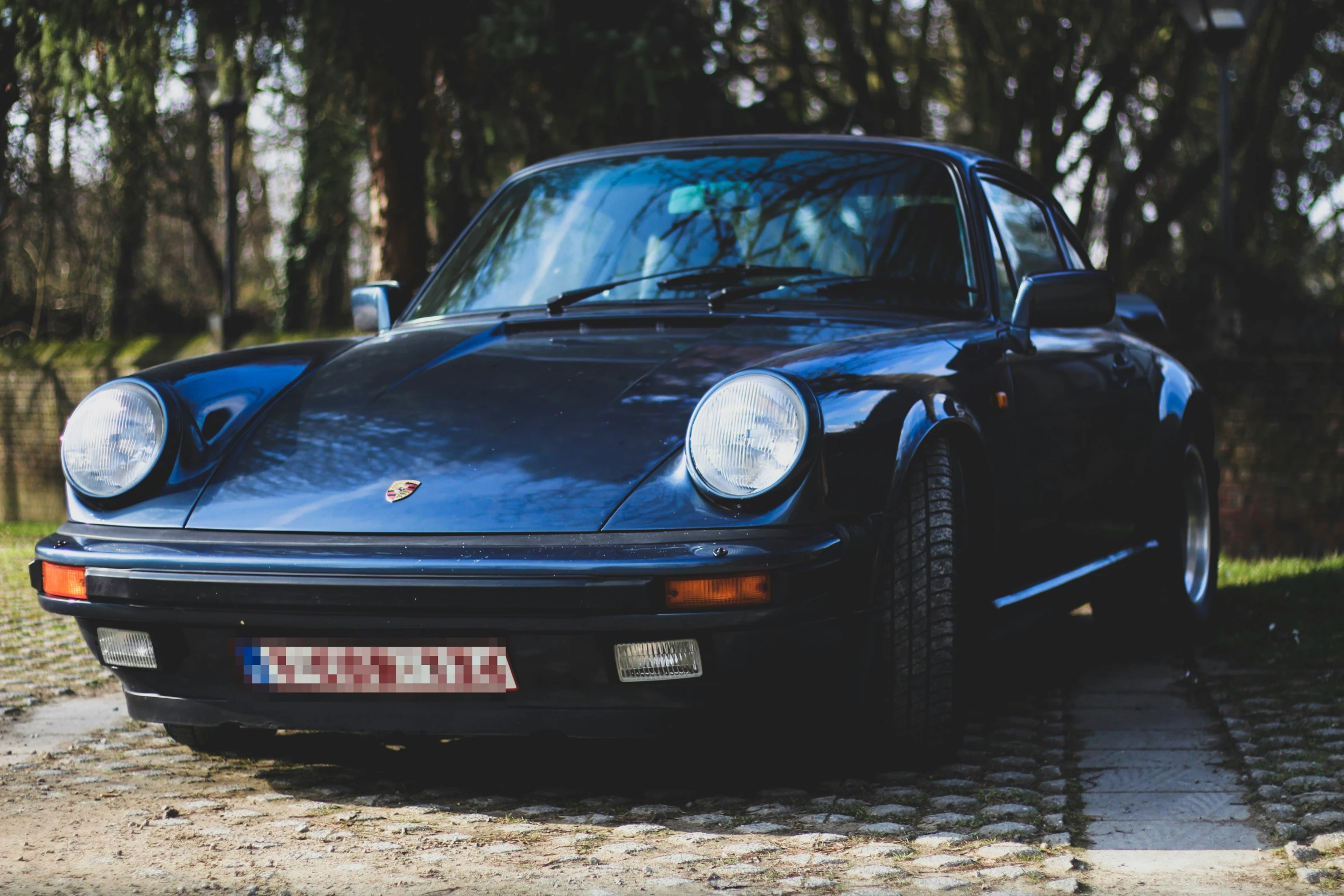 an old black porsche parked near some trees