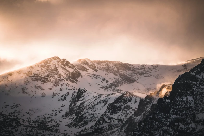 snow - capped mountains under a partly cloudy sky in the evening