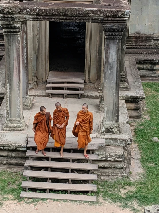 three monks in orange robes sit on stairs