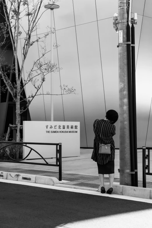 black and white pograph of a person leaning against a pole near the ocean