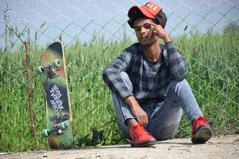 a skateboarder sitting down beside a fence while talking on his cell phone