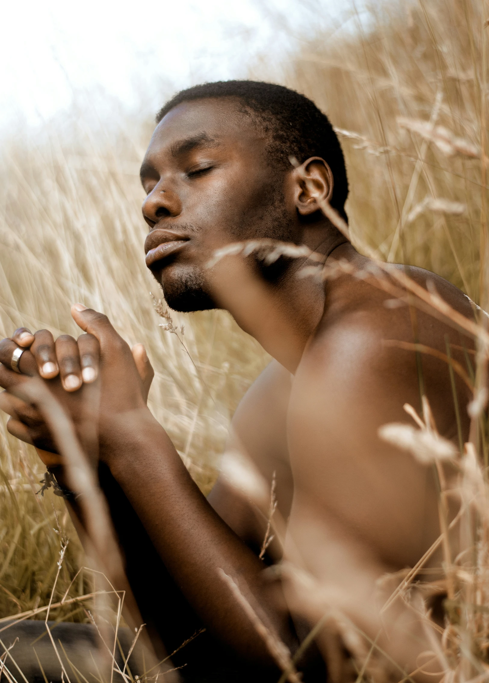 man kneeling in grassy area with hands crossed, praying