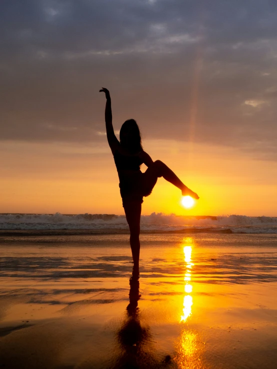 woman standing on beach in front of sunset with arms in air