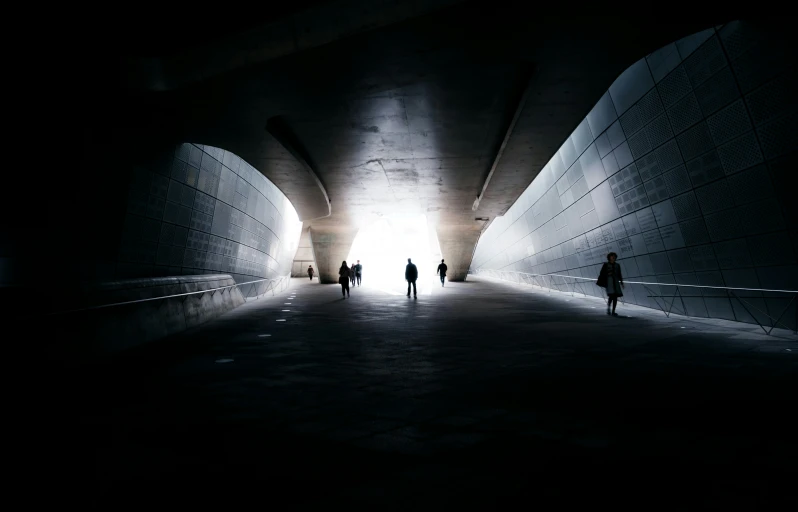 people walk through an underground tunnel with light at the end