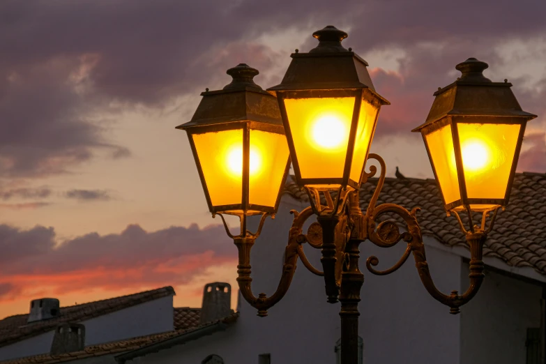 two lights on an old fashioned post in front of a sunset