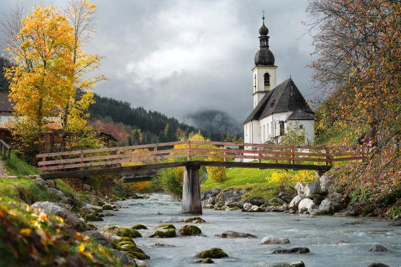 a church stands alone beside a stream and bridge