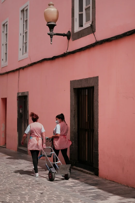 two people with a baby carriage walking past a pink building