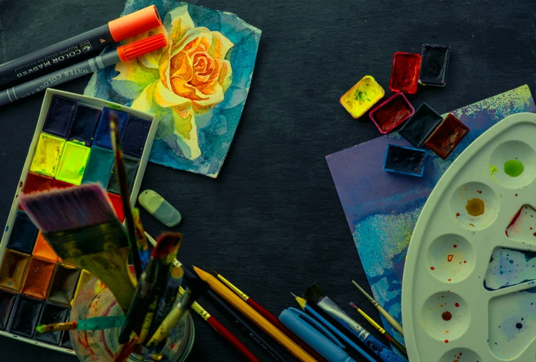 different colored paints, brushes and other supplies are placed on a black surface