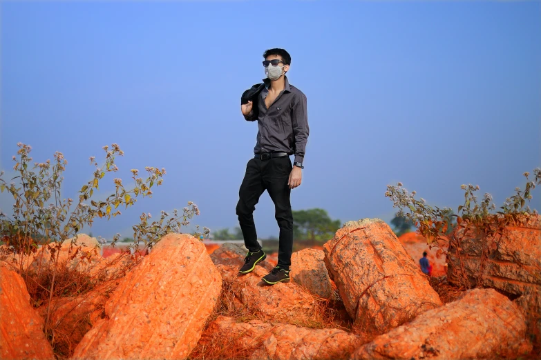 the man is standing on large rocks with sunglasses on his face