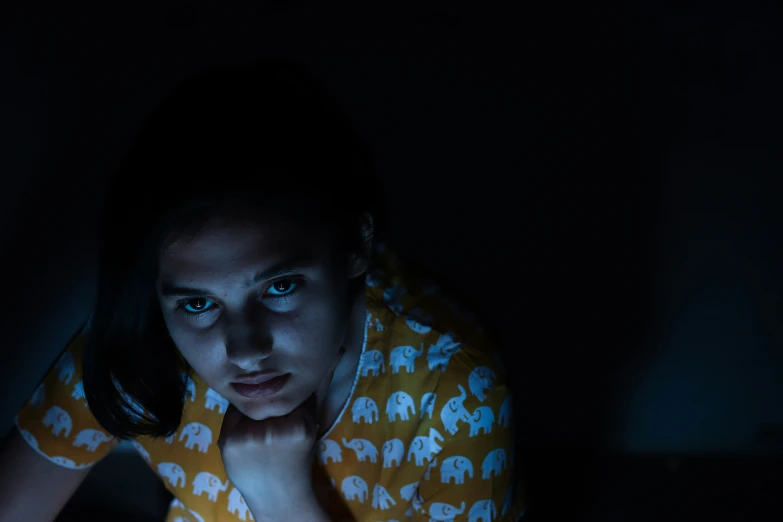 a girl in a yellow shirt holding a laptop in the dark