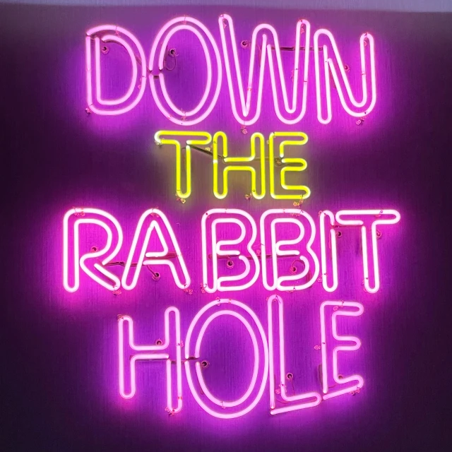 a neon sign reading down the rabbit hole