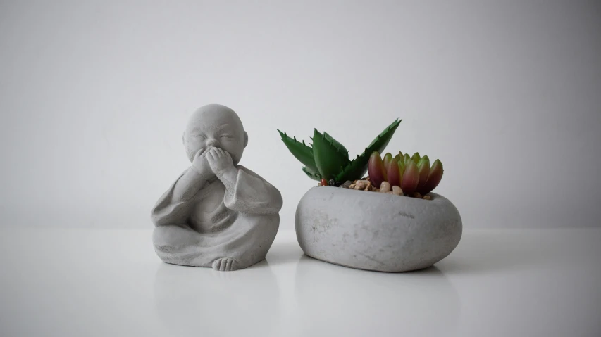 a statue holding his hands behind his face, with a succulent in a bowl on his lap