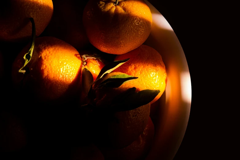 a bowl filled with ripe oranges with leaves