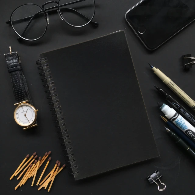 a notebook, pencils and watch lay on top of a table