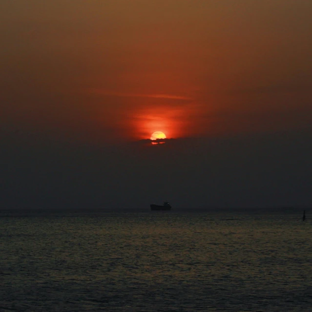 the sun sets over the water with a ship in the distance