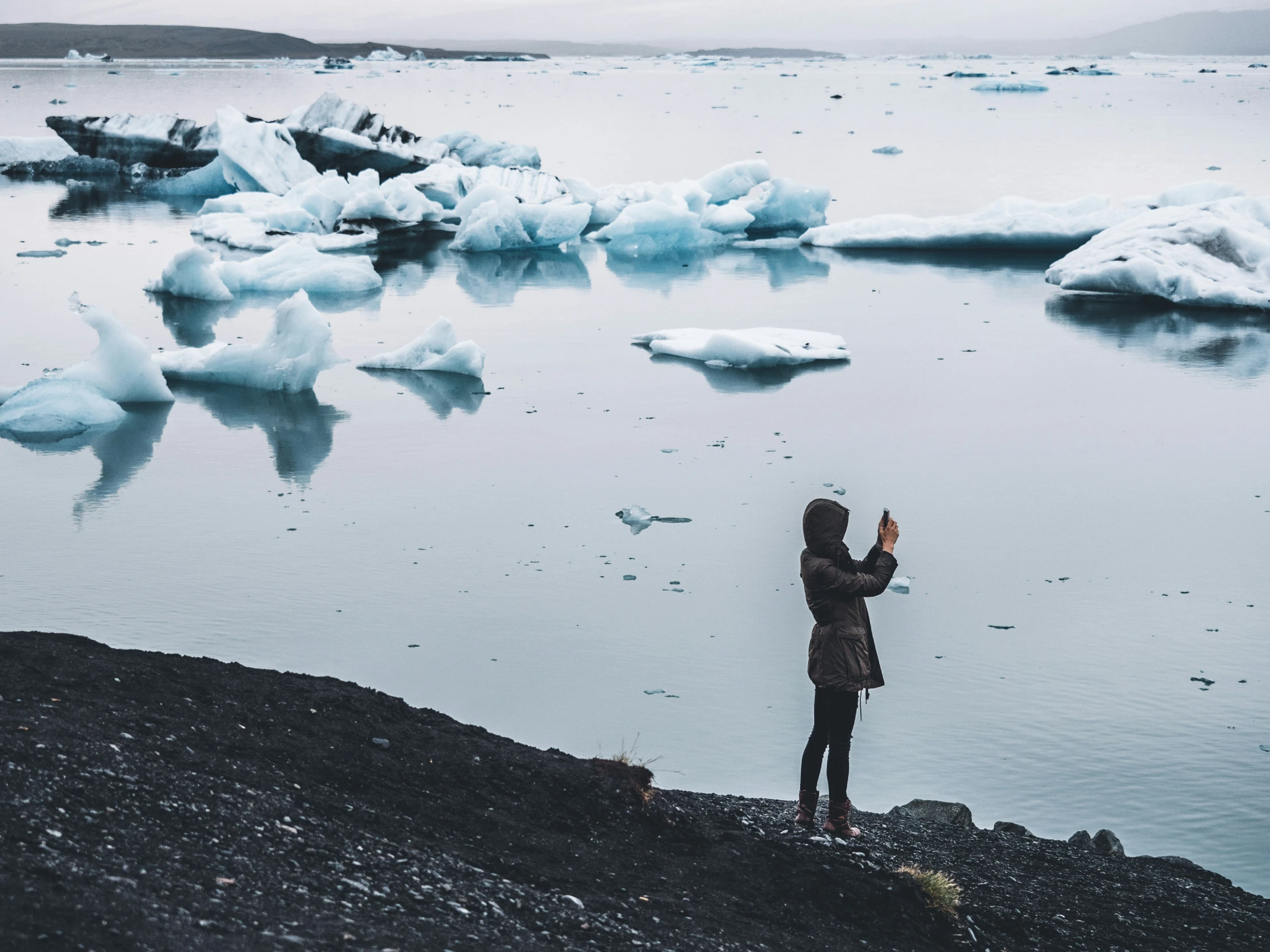 the girl is standing on rocks and looking at some icebergs