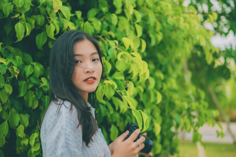an asian woman in front of trees holding a camera